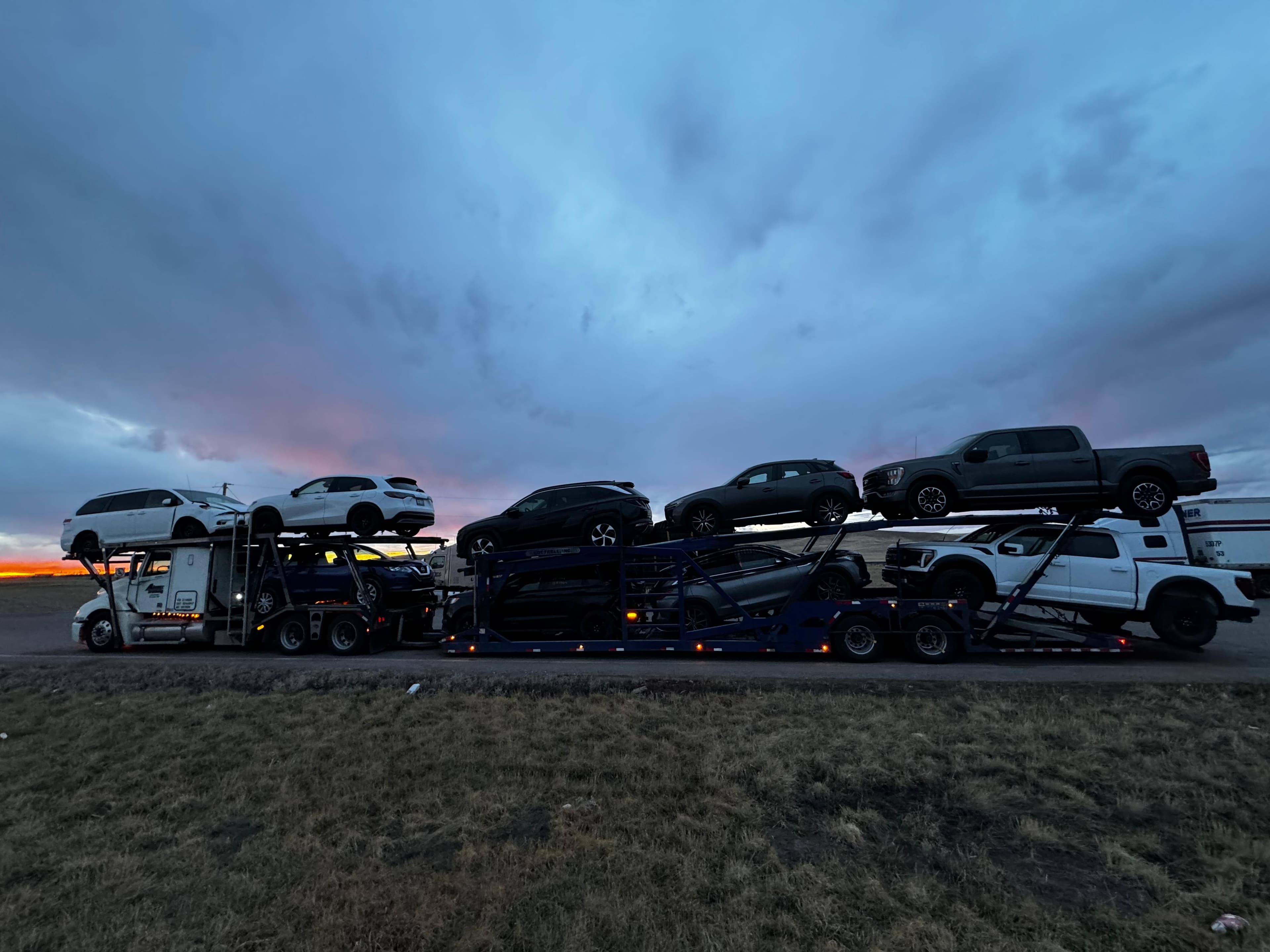 Prairie Auto Transport carrier hauling vehicles across the Canadian prairies at sunset